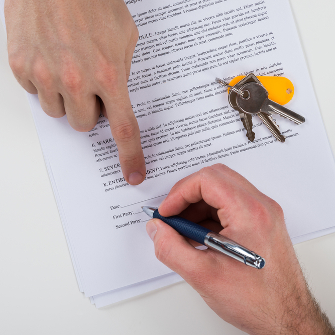 a person signing a rental agreement with a set of keys on it